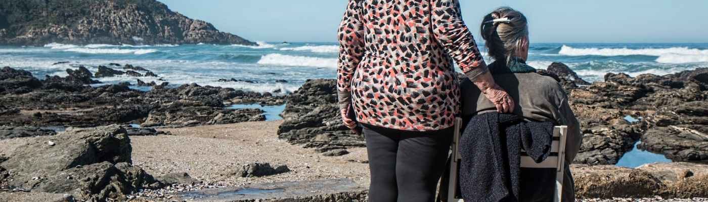 woman standing beside woman on white wooden chair facing body of water