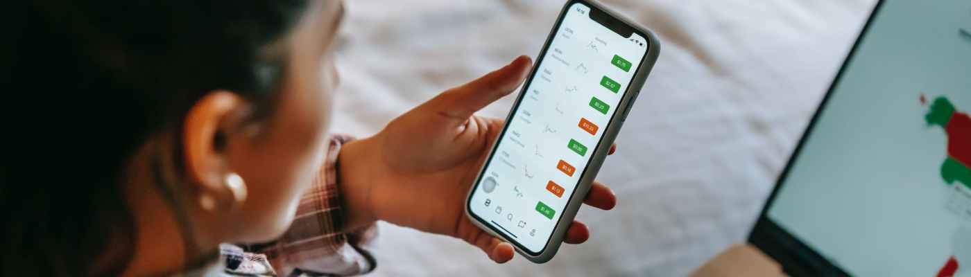 crop ethnic analyst using trading application on smartphone on bed