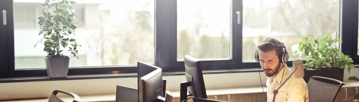 man with headphones facing computer monitor