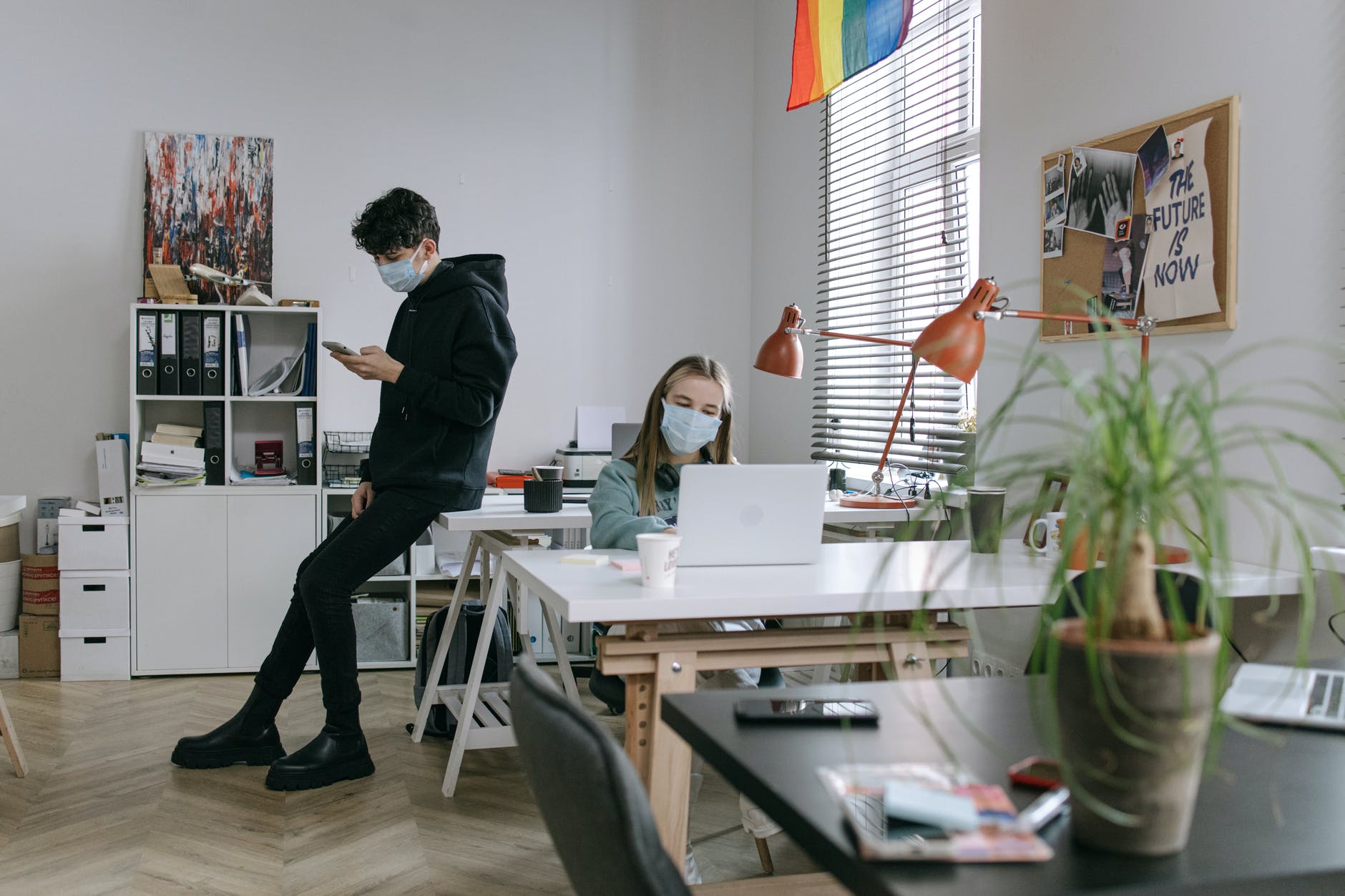 man in black hoodie jacket sitting on office table and woman using her laptop
