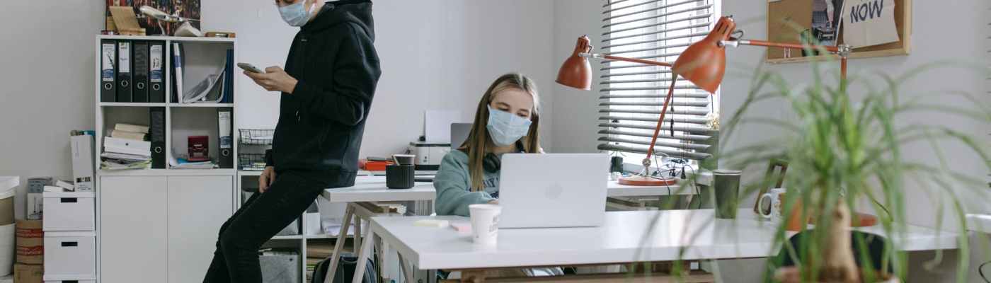 man in black hoodie jacket sitting on office table and woman using her laptop