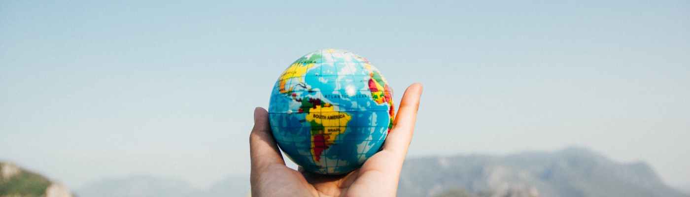 person holding world globe facing mountain