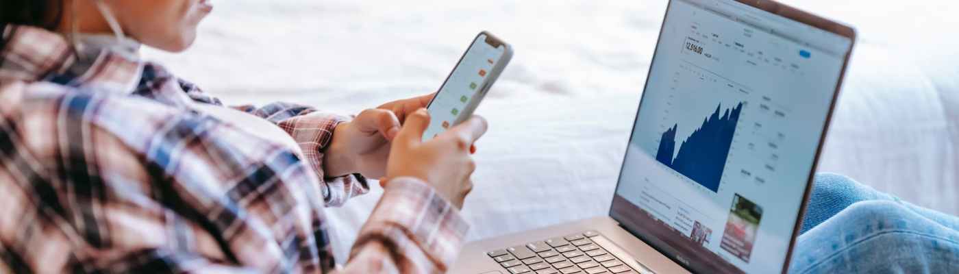 crop ethnic trader with smartphone and laptop on bench indoors